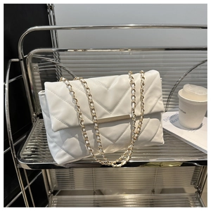 Close-up of white V-quilted flap bag with gold metal buckle on modern shelf display