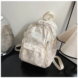 Detail view of beige nylon backpack featuring hand-drawn bear patterns and logo patch