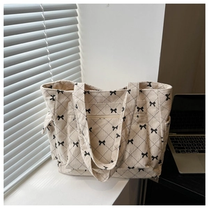 Close-up of beige corduroy tote bag featuring quilted patterns and black ribbon bows