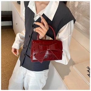 Detail of burgundy patent leather handbag featuring a large bow and glossy crinkled texture