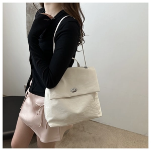 Close-up of beige PU leather backpack with silver metal turn-lock and soft pleat texture