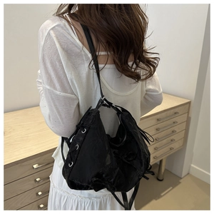 Détail du sac cabas en satin noir avec œillets argentés et nœuds sur l'épaule du modèle