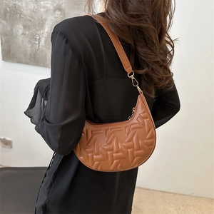 Brown half-moon shoulder bag with woven embossed texture and leather strap shown on model