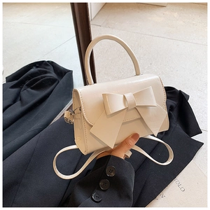 Close-up of a stylish cream mini handbag with a large bow on a black blazer