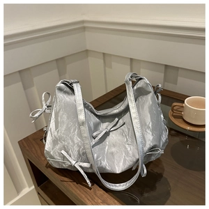Détail du sac cabas argenté métallisé avec rubans décoratifs sur table vitrée