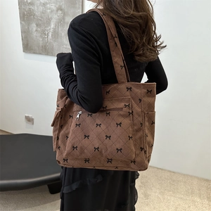Brown corduroy tote bag with bow prints and wide straps shown on a model side view