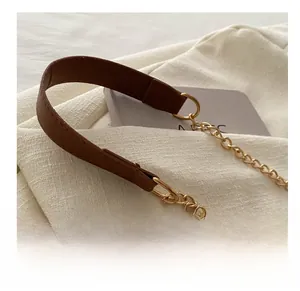Detail of a brown leather shoulder strap with a gold metal chain on white textured fabric