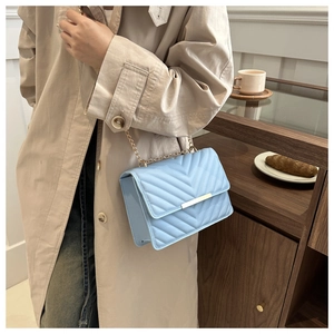 Quilted light blue crossbody bag with gold chain strap shown in a lifestyle setting