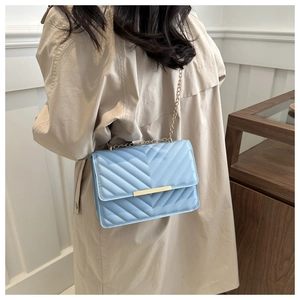 Detailed side view of a light blue V-quilted crossbody bag with a gold chain strap
