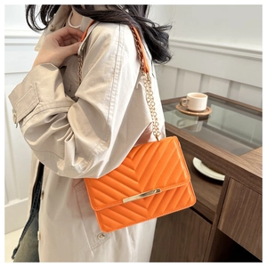 Detail of bright orange quilted crossbody bag with golden chain strap and hardware lock