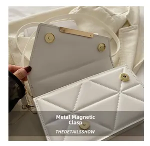 Detail of white quilted crossbody bag with golden hardware magnetic buckle closure