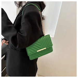 Detail of green chevron quilted crossbody bag with a gold chain strap on a model