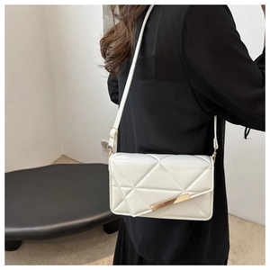 Detail view of a white quilted geometric crossbody bag with gold accents on a model