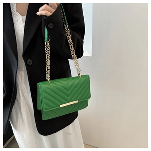Detail of green quilted shoulder bag with V-shaped stitching and gold metal chain strap