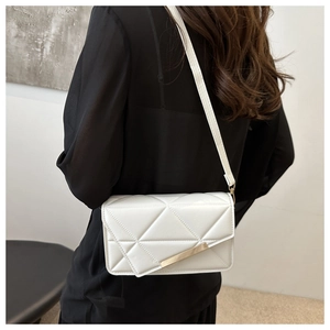 Close-up of white quilted crossbody bag with gold metal trim worn by model