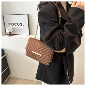 Detail of brown V-quilted shoulder bag with gold chain strap worn by a model