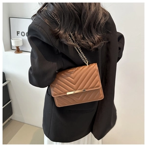 Detail view of brown quilted chain bag with V-stitch pattern and golden metal bar