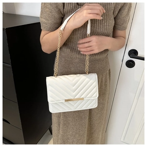 Detail of white V-quilted crossbody bag with gold hardware and chain strap