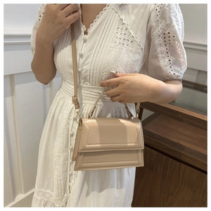 Elegant beige crossbody bag with geometric design worn by model in a white lace dress