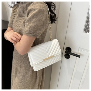Close-up of white quilted crossbody bag with gold chain strap worn by a model