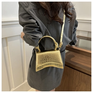 Detail of gold crocodile embossed mini handbag with curved base on model in grey suit