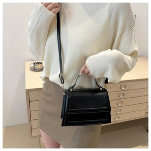 Detail of a structured black crossbody bag with gold buckle and layered front flap design