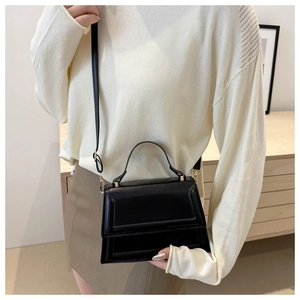 Detail of a structured black mini crossbody bag with gold hardware and top handle