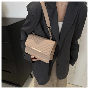 Detail of beige quilted crossbody bag with V-shaped texture and gold chain on gray blazer
