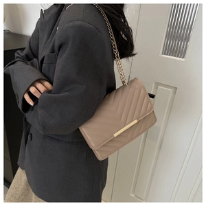 Detail view of beige crossbody bag with chevron quilting and gold metal accent