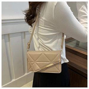 Side view of model wearing a beige quilted crossbody bag with gold metal bar detail