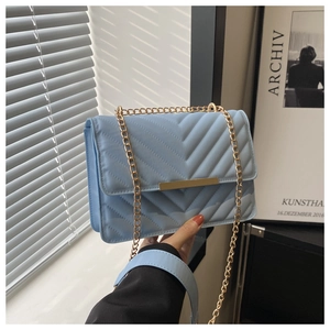 Detail of light blue quilted crossbody bag with gold chain strap and metal clasp