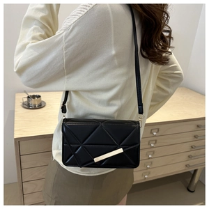 Detail of black crossbody bag with geometric quilting and gold hardware on model