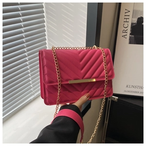 Close-up of rose red quilted small square bag with V-shaped stitching and gold metal bar