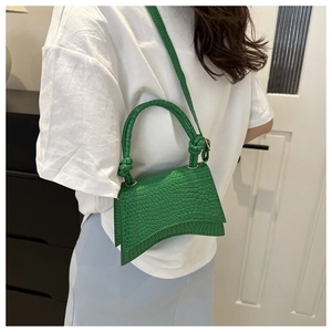 Bright green crocodile pattern handbag with knot detail and curved bottom shown on a model