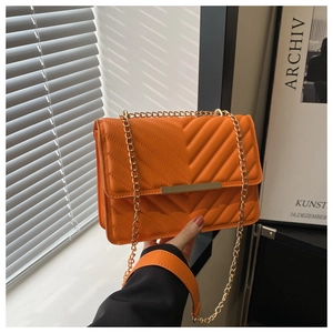 Close-up of bright orange V-quilted shoulder bag with gold metal bar and chain strap