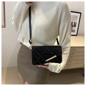 Detail of black quilted crossbody bag with gold metal trim and adjustable strap on a model