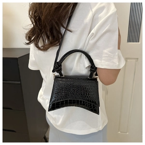 Detail of black hourglass handbag with crocodile texture and unique curved base on model