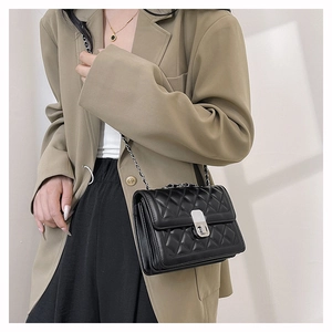 Detail shot of a black quilted crossbody bag with silver chain strap worn on a blazer