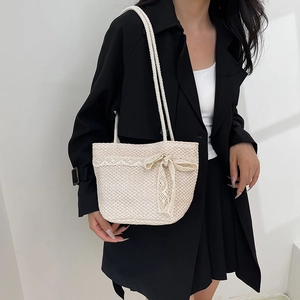 Minimalist beige woven tote bag with lace bow detail worn over a black trench coat