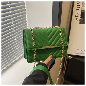 Close-up of green leather crossbody bag with V-shaped chevron quilting and gold chain