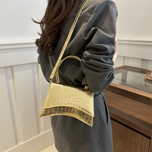 Golden crocodile embossed hourglass handbag with adjustable strap shown on shoulder