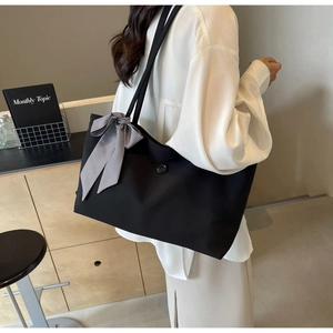 Detail of black tote bag with checkered bow and round button on a shoulder strap