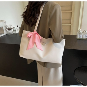 Detail of white tote bag with pink plaid bow accent worn on shoulder in a cafe