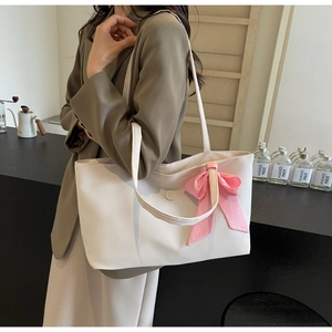 Detail of white leather tote bag featuring a large pink plaid bow and metal logo charm