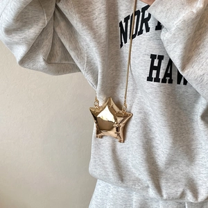 Metallic gold star-shaped crossbody bag with slim chain strap worn over a grey hoodie