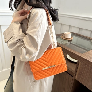 V-quilted bright orange crossbody bag with gold chain strap worn by a female model