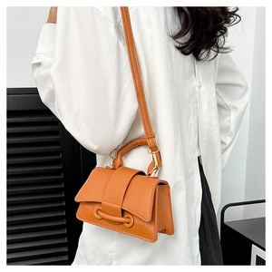 Detail of caramel orange crossbody bag with lychee texture and buckle strap on white shirt