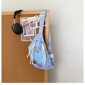 Detailed view of light blue quilted chest bag with colorful embroidery and star charms