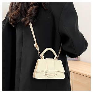 Detail of cream crossbody bag with lychee texture and gold hardware on a black blazer