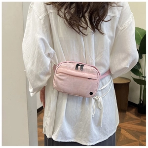 Close-up of a light pink crossbody waist bag featuring dual black metal zippers and nylon fabric